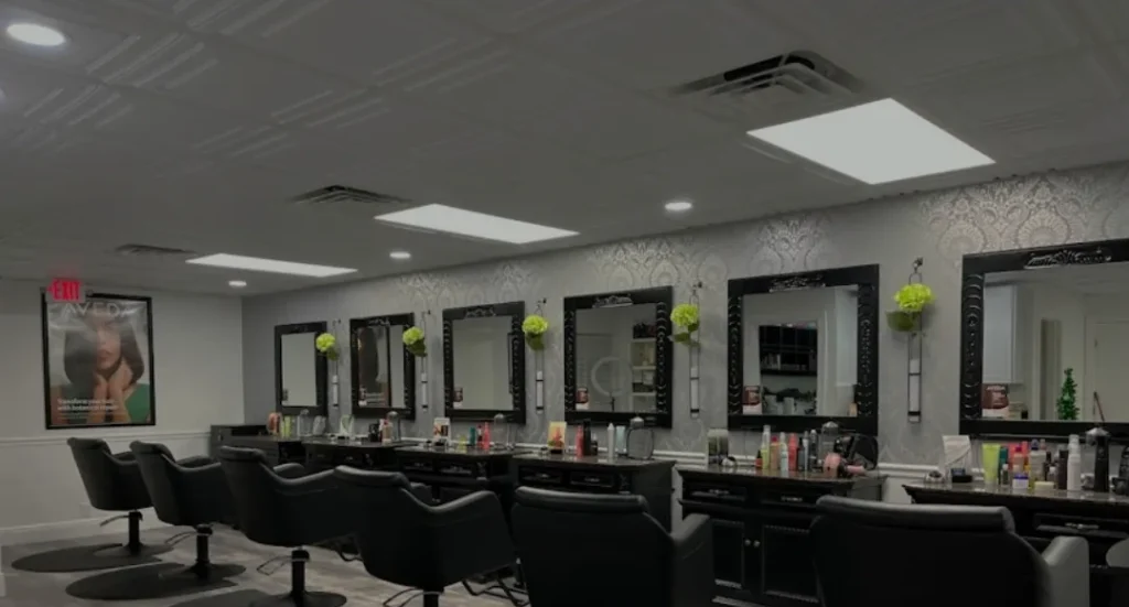 A row of black salon chairs facing large mirrors and countertops with hair products in a well-lit modern beauty salon.