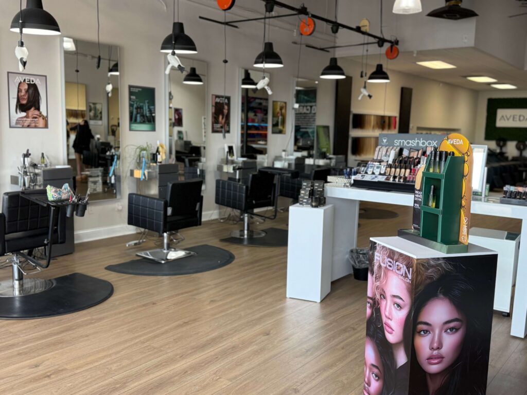 A modern hair and beauty salon with black styling chairs, large mirrors, product displays, and beauty posters on white walls.
