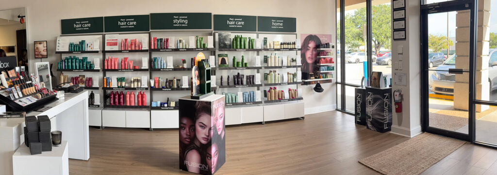 A modern hair care store interior with shelves of hair products, large product posters, and natural light coming through glass doors and windows.