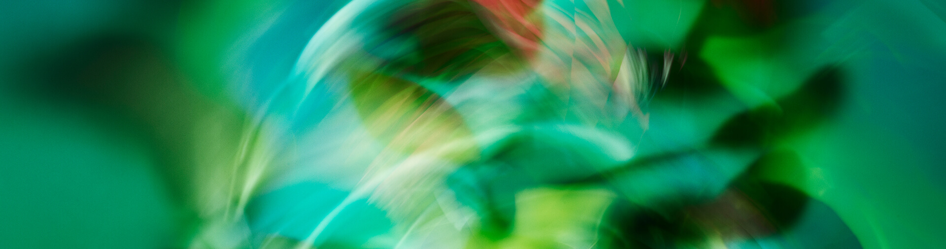 Abstract image with blurred shapes and swirls in green, blue, red, and yellow tones, creating a sense of motion and layered color.